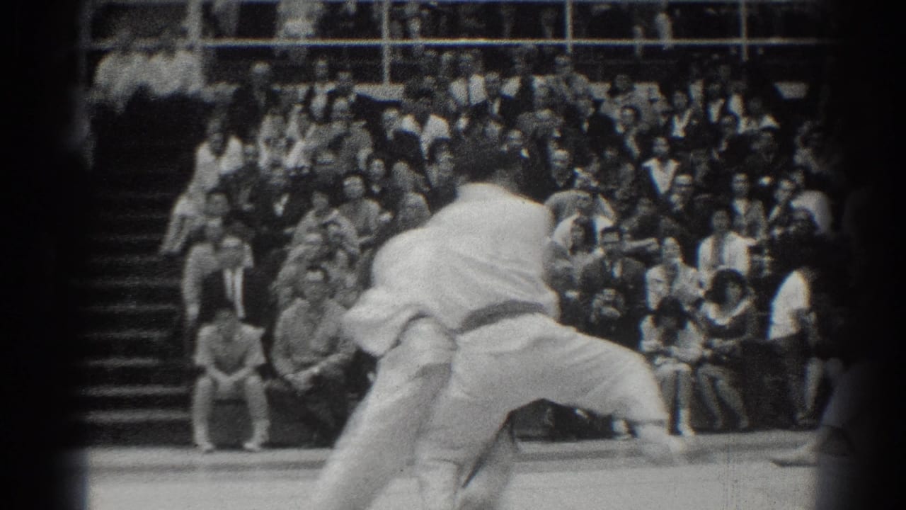 In the supplied 1966 West Covina context, two karate competitors in white gi grapple at close range while spectators fill the bleachers behind them.