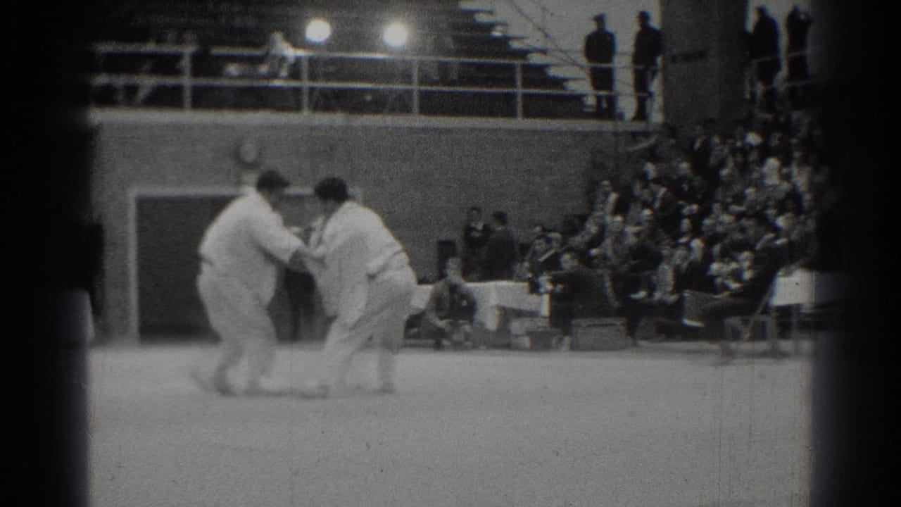 Two judo competitors face each other on a mat before a seated audience.