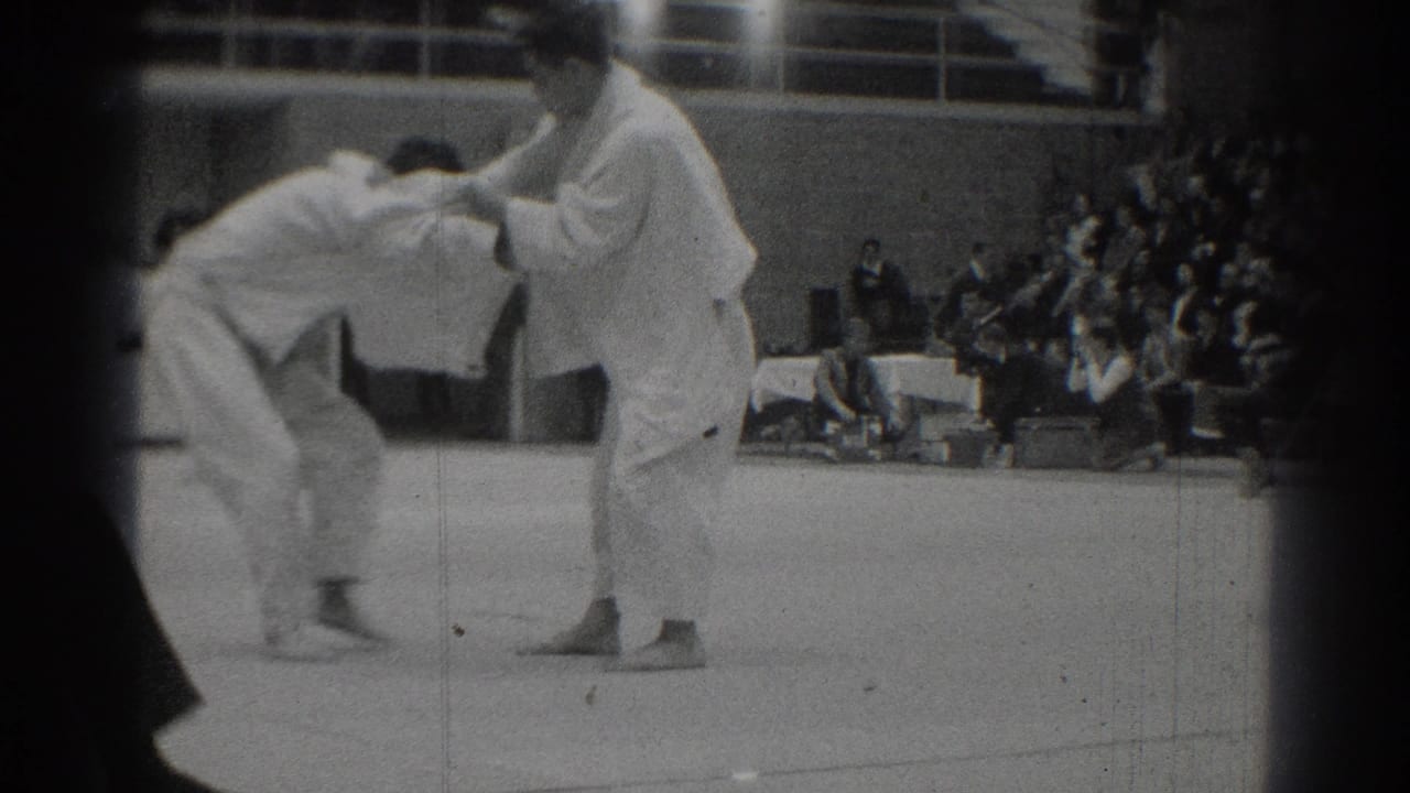 1966 West Covina home-movie frame showing two judo athletes beginning a grip exchange on an indoor competition mat.