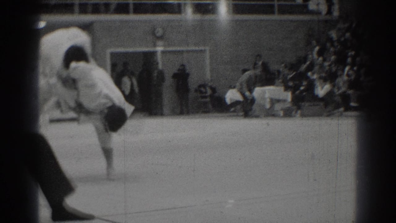 1966 West Covina footage shows a judo exchange mid-motion, partly obscured by the film frame edge and audience seating.