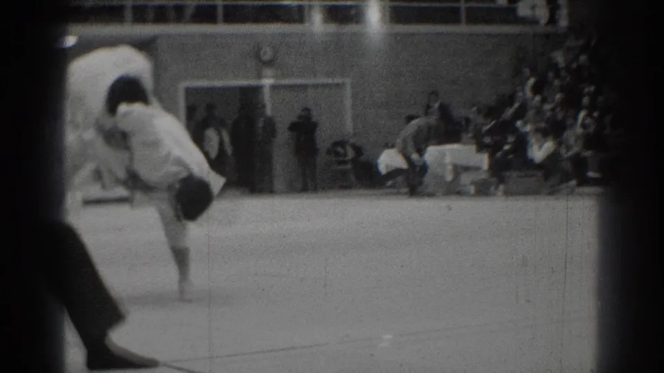 1966 West Covina footage shows a judo exchange mid-motion, partly obscured by the film frame edge and audience seating.