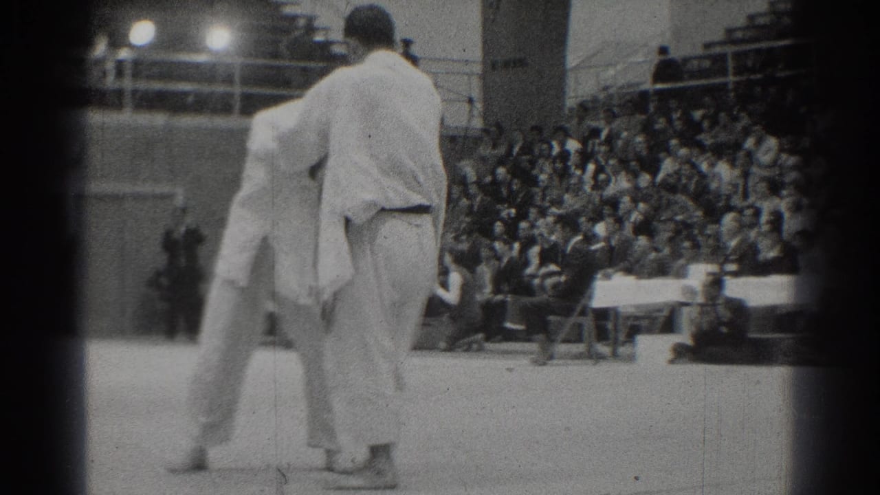 In 1966 West Covina footage, two adult competitors in white gi uniforms face each other on a mat with bleachers behind them.