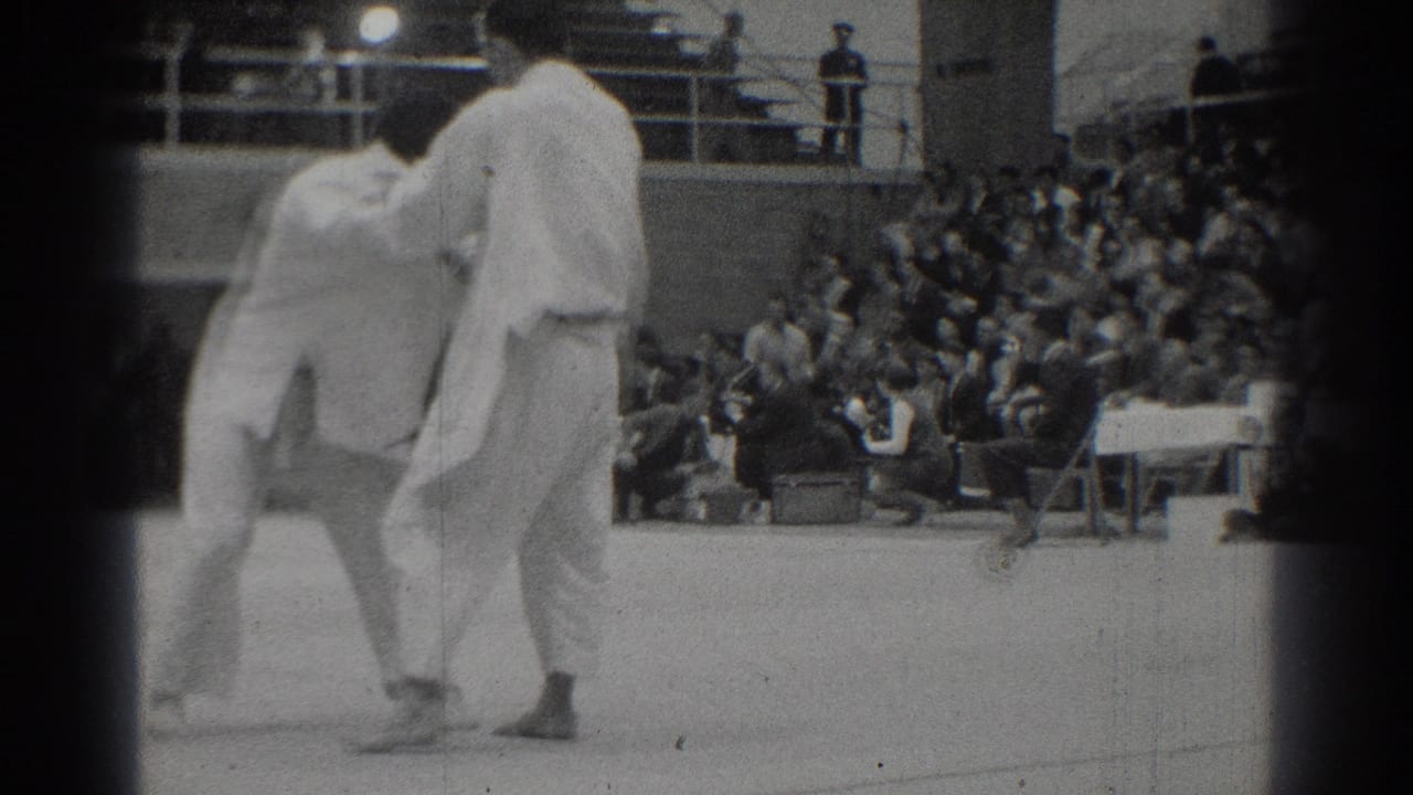 The West Covina martial arts match continues as two adult men in white gi uniforms shift position before the bleacher crowd.