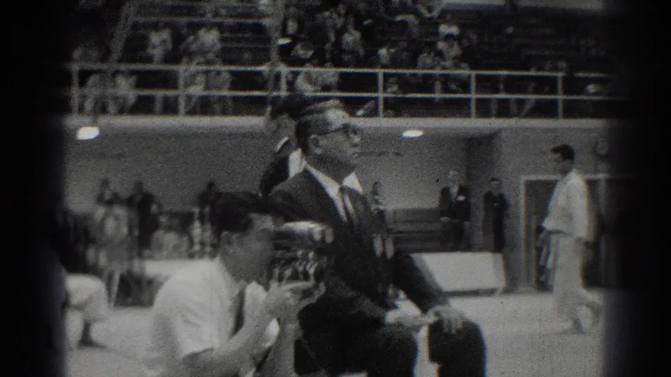 A suited official or judge sits beside the competition area during the 1966 indoor martial arts event in West Covina.