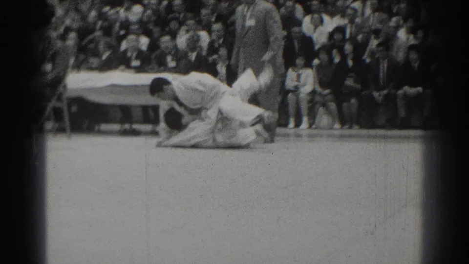 A gi-clad competitor appears to complete a throw or takedown on the indoor mat as the crowd watches in West Covina.