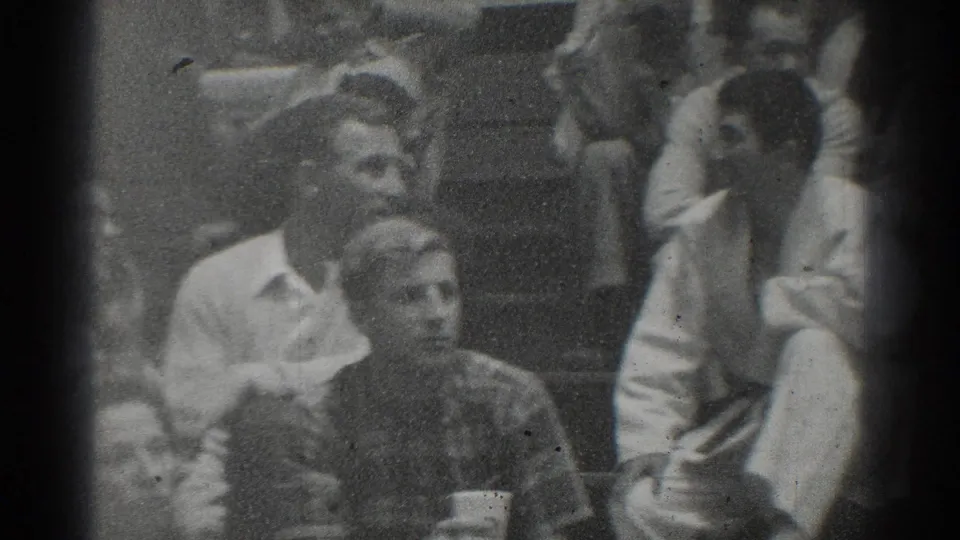 Spectators at the West Covina judo event sit close together, with faces visible in soft black-and-white 8mm footage.