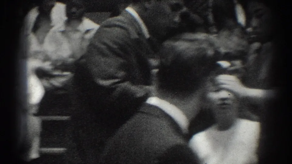 Close spectator view from the 1966 West Covina judo event, showing men in suits and nearby attendees seated in a crowded room.