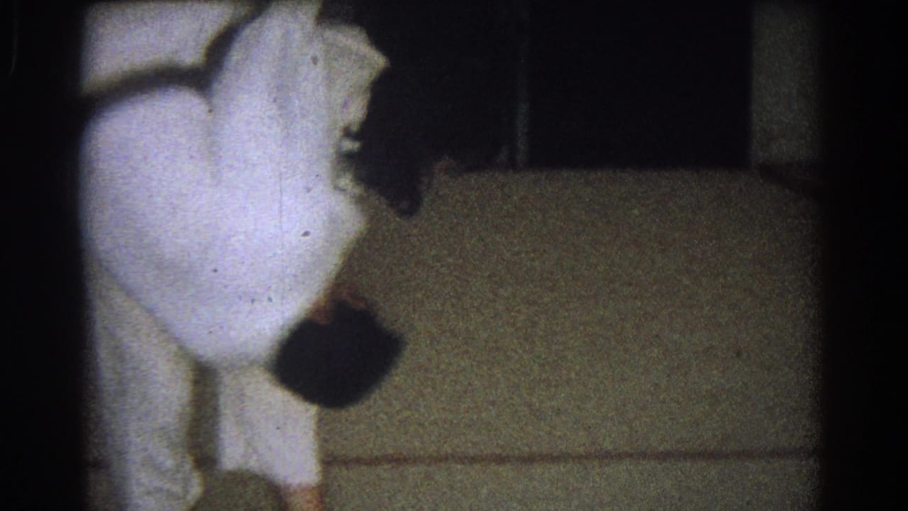 Two people in white martial arts uniforms grapple near a mat in a dark interior.