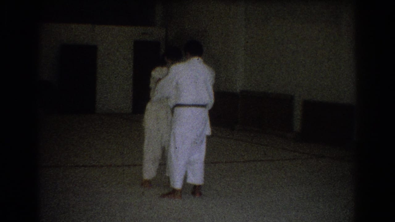 Two adults in white martial arts uniforms stand on an indoor mat in West Covina, California, seen from behind during practice.