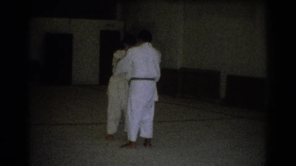 Two adults in white martial arts uniforms stand on an indoor mat in West Covina, California, seen from behind during practice.