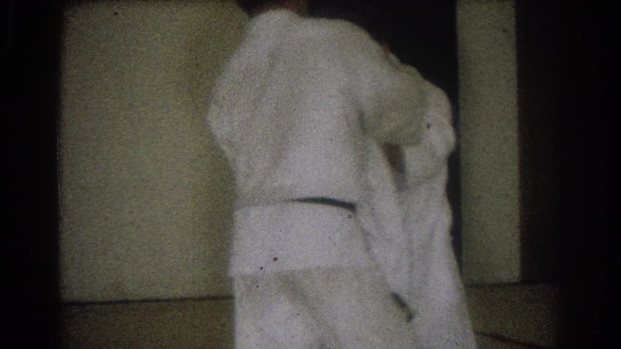 Two men in white gi remain close after a grappling move, with one bent forward in a dim West Covina indoor practice space.