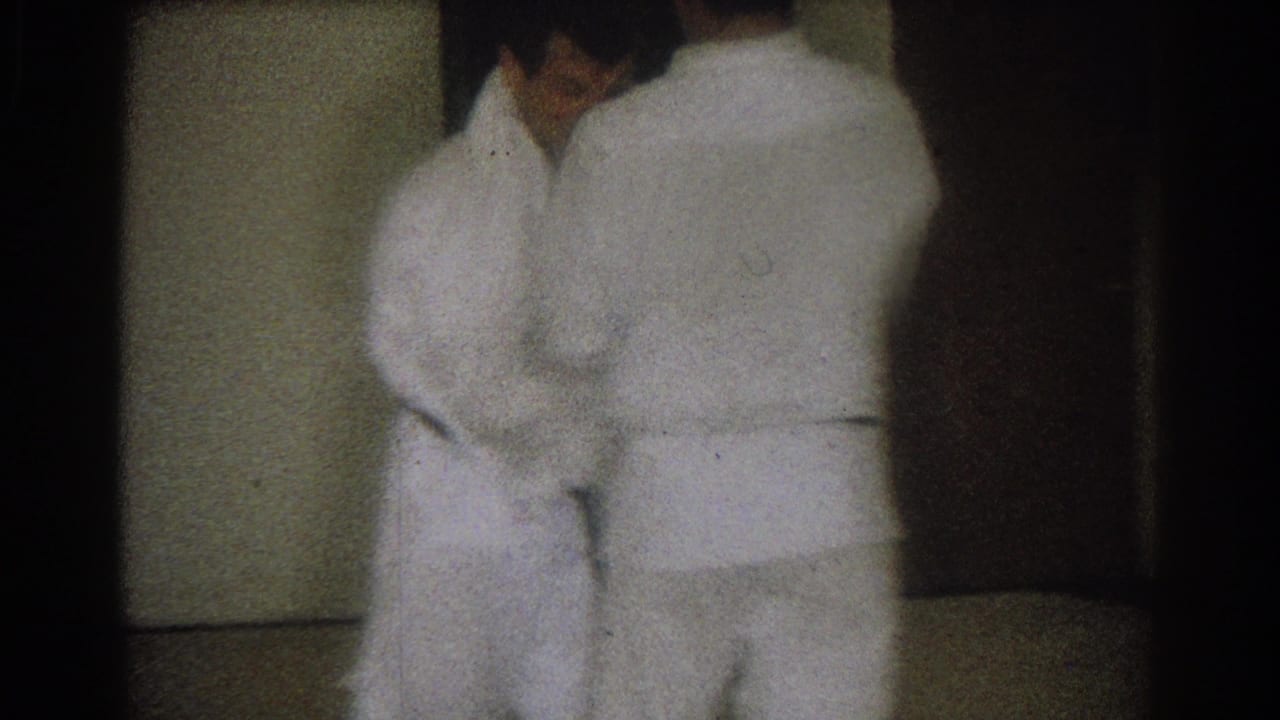 Two adult men in white judo uniforms practice at close range indoors, from 1966 West Covina home-movie footage.