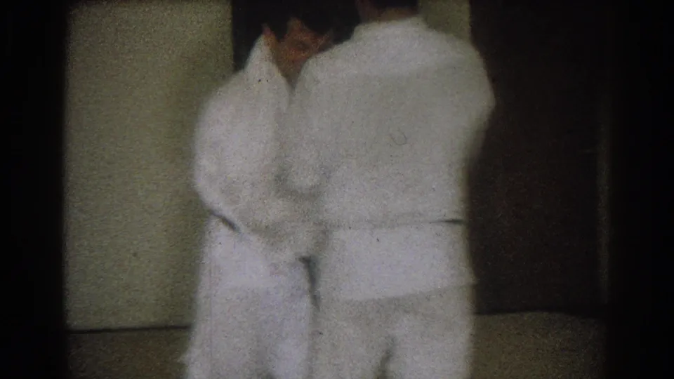Two adult men in white judo uniforms practice at close range indoors, from 1966 West Covina home-movie footage.