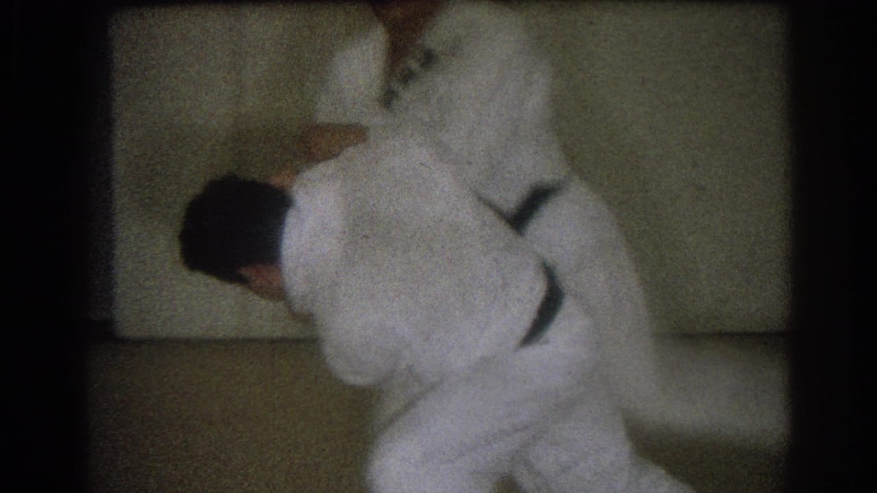 Two men in white judo uniforms grapple on a dojo mat.