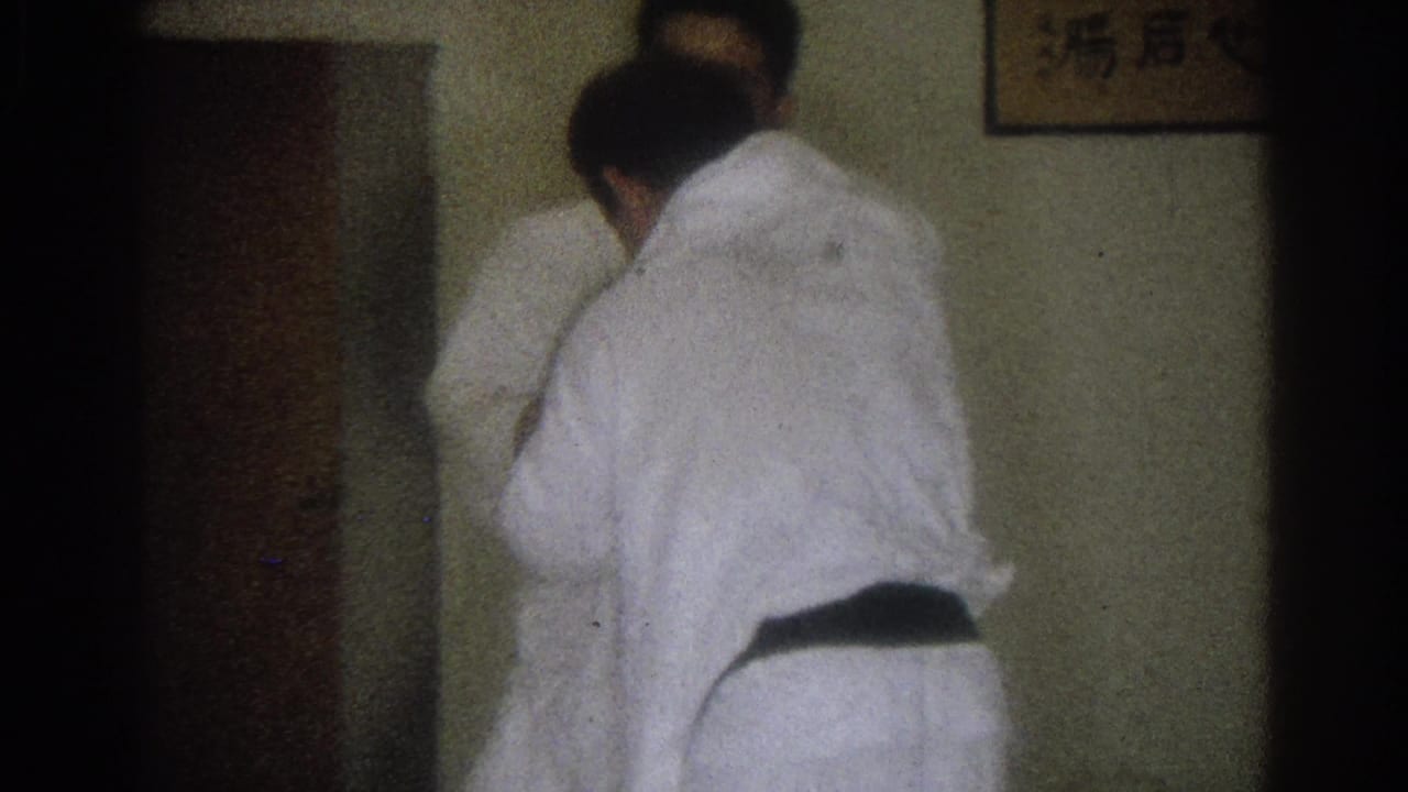 Inside the West Covina dojo, one man in a white gi turns through a grappling movement while another practitioner is partly hidden nearby.