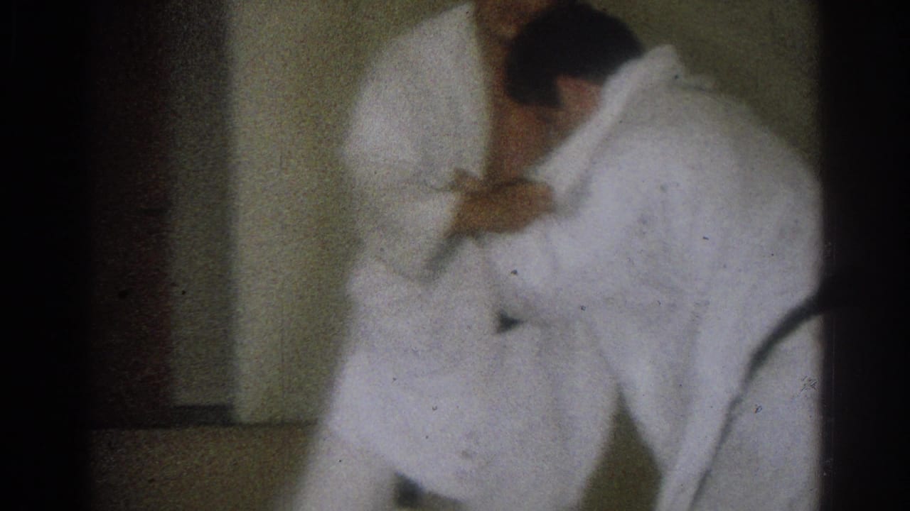 Two adult men in white judo uniforms work through a close grappling hold in the 1966 West Covina dojo home movie.