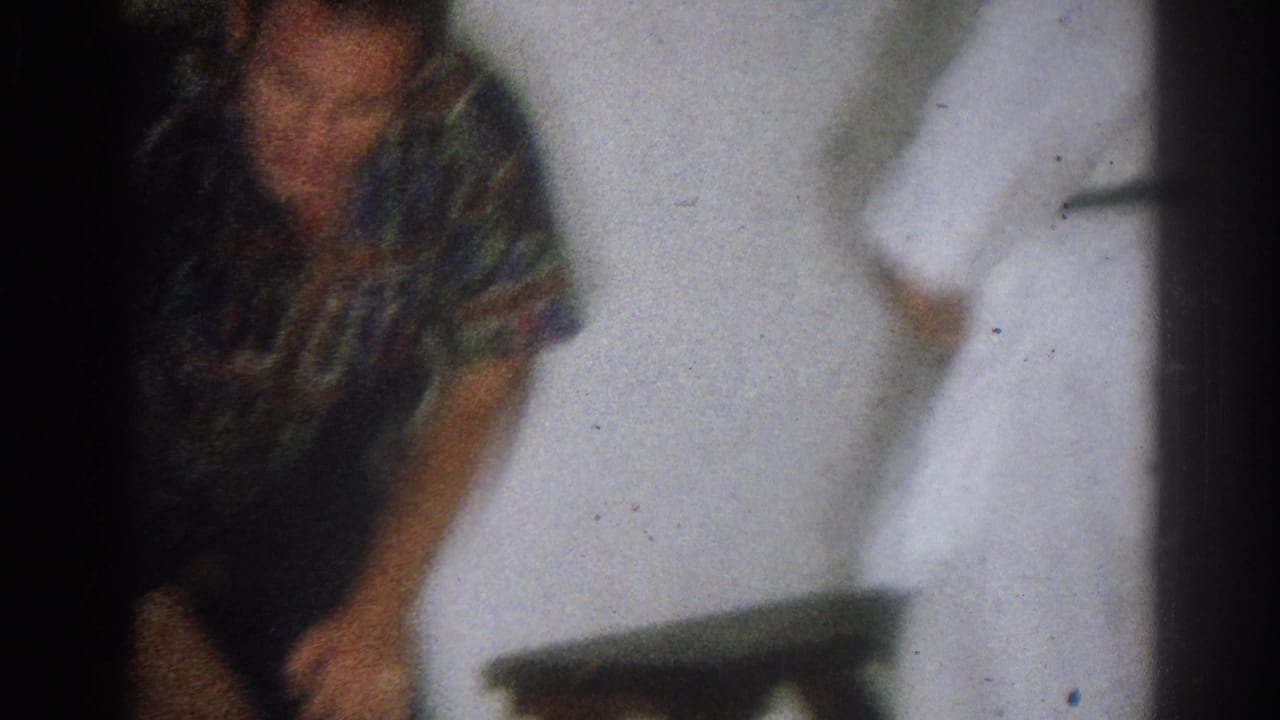 1966 West Covina home-movie frame with blurred handheld framing of the instructor and student near a white wall.