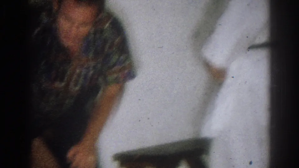 1966 West Covina home-movie frame with blurred handheld framing of the instructor and student near a white wall.