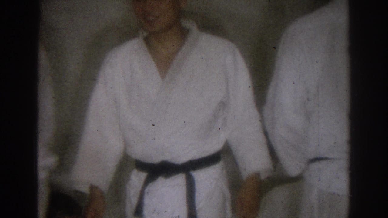 Soft 8mm frame from a 1966 West Covina martial arts session, with a black belt practitioner facing the camera beside another participant.