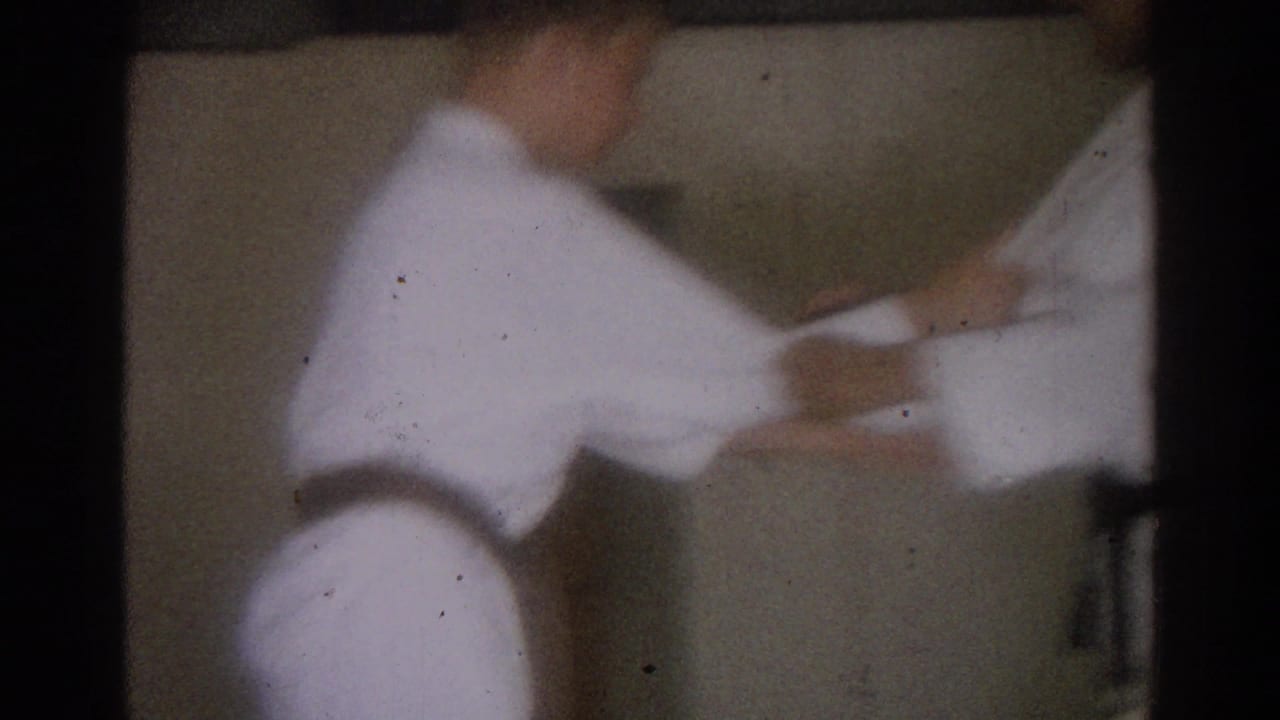 Two men in white karate uniforms practice a hand technique indoors.