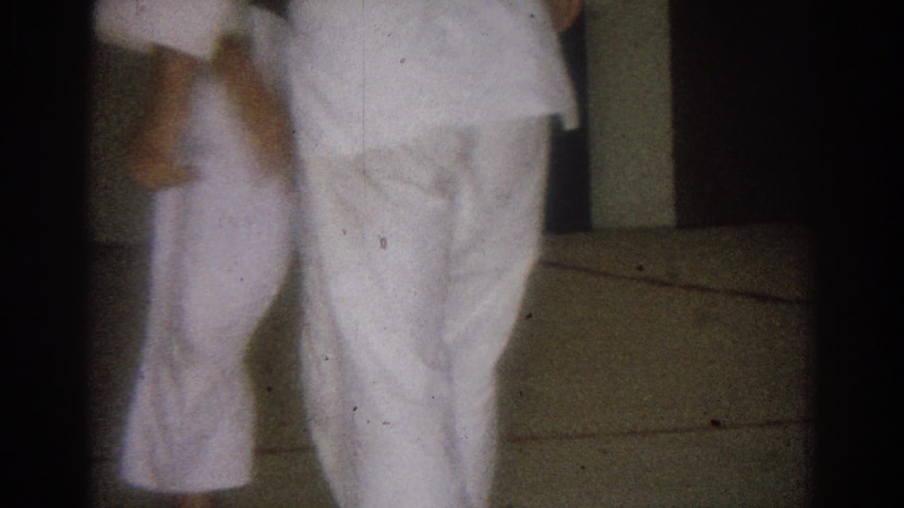 The frame shows the lower bodies of two men in white gi as they shift stance during the 1966 indoor karate practice.