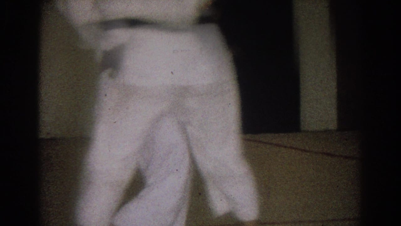Blurred close view of a white karate gi near a dim dojo mat.
