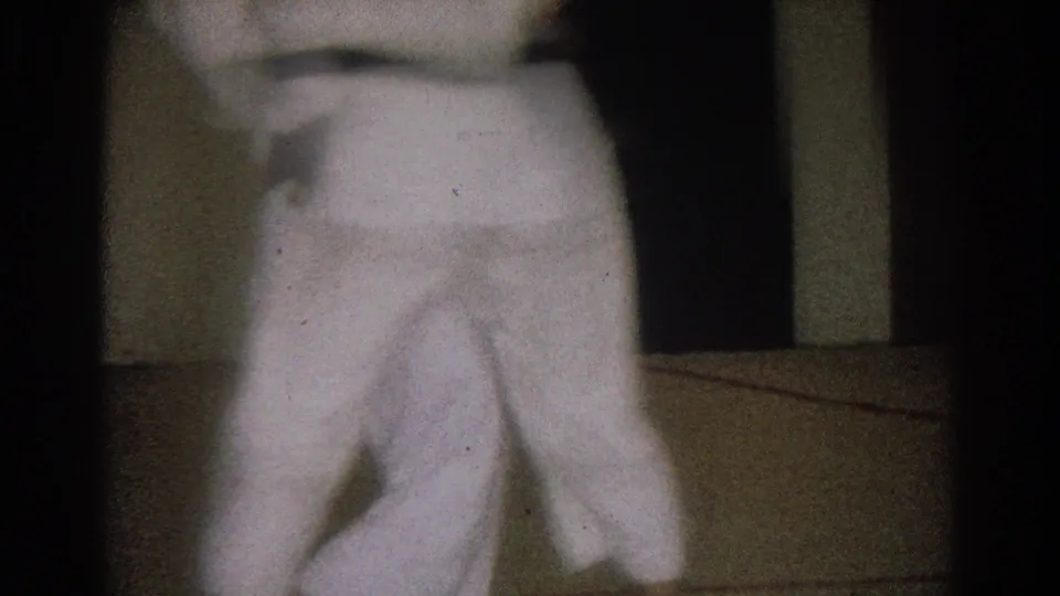 Soft 8mm frame from 1966 West Covina showing a close, blurred view of a white karate gi beside a dim mat area.