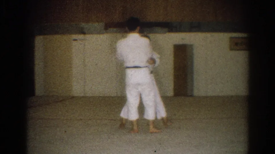 In the 1966 West Covina dojo footage, one man in a white gi faces away while another is partly visible during practice.