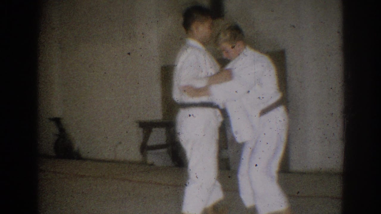Two black-belt judo practitioners work through a close grappling position inside the simple West Covina training room.