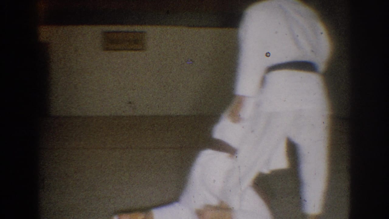 Late frame from the 1966 West Covina clip shows one student bent low as another stands during a martial arts practice technique.