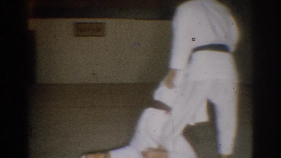 Late frame from the 1966 West Covina clip shows one student bent low as another stands during a martial arts practice technique.