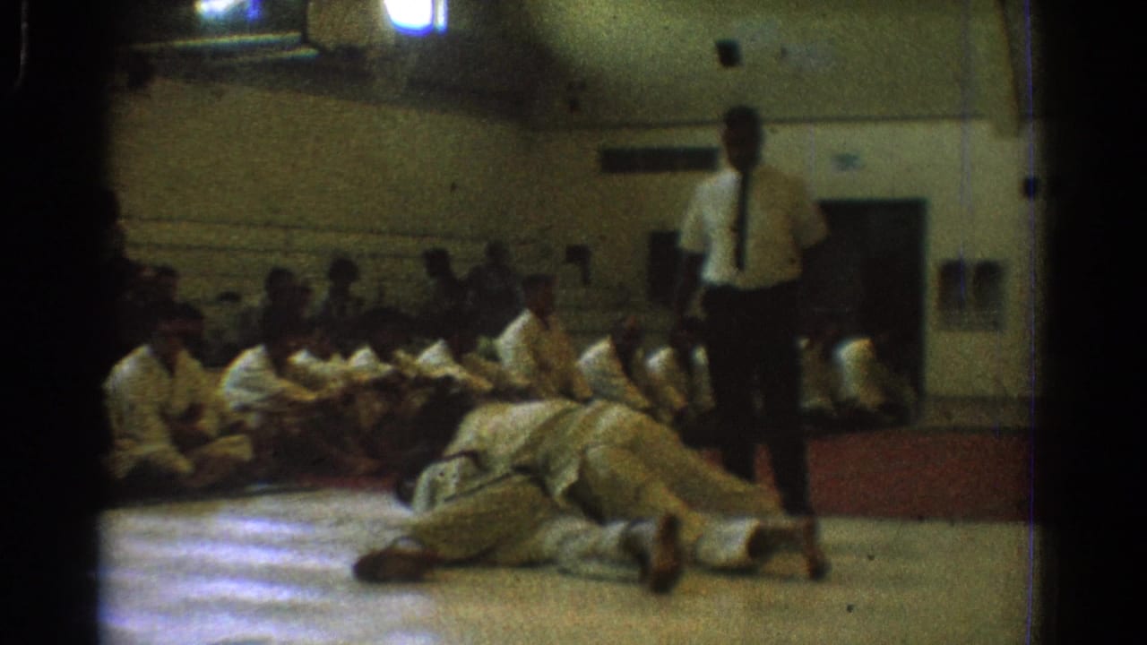During the West Covina gymnasium match, the two gi-clad participants are on the mat with the referee standing over the action.