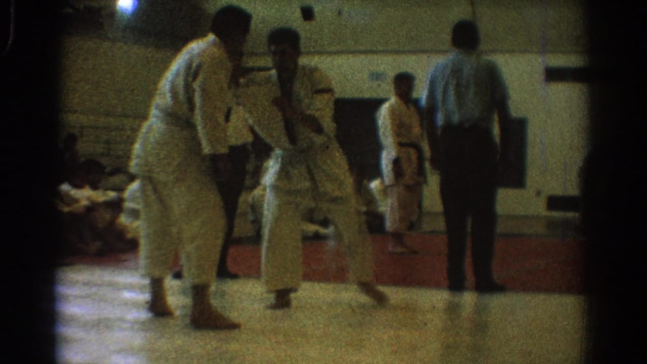 In the 1966 West Covina gym footage, one competitor closes distance while the referee watches from the mat edge.