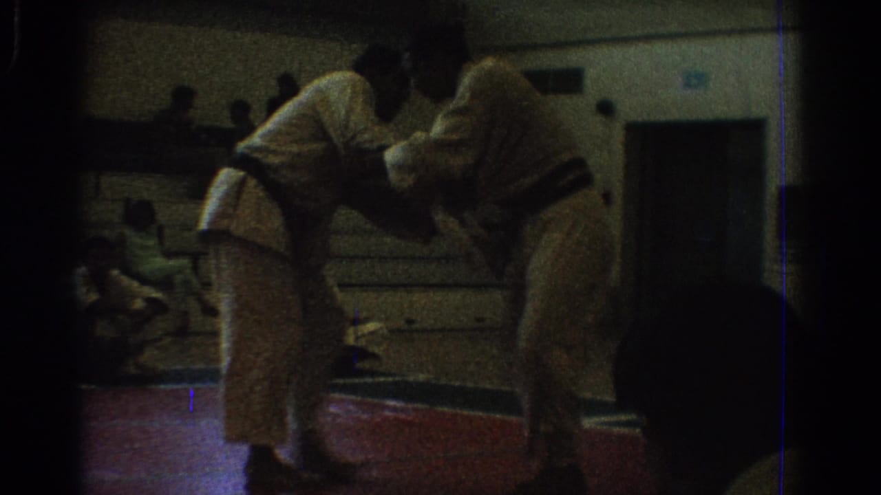 A low-light 8mm frame shows two martial artists working a close hold during the West Covina gym competition.