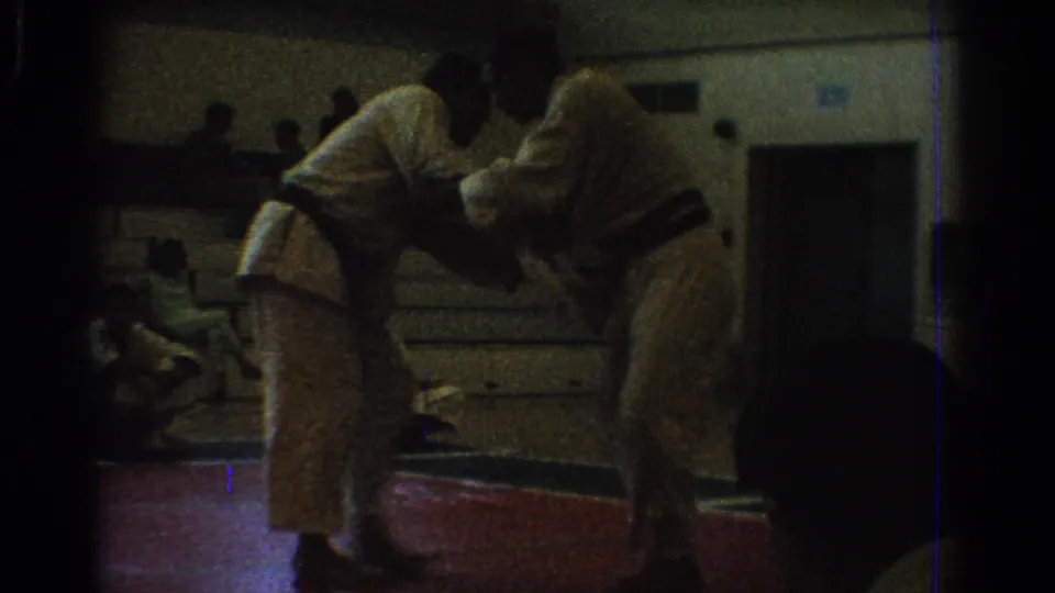 A low-light 8mm frame shows two martial artists working a close hold during the West Covina gym competition.