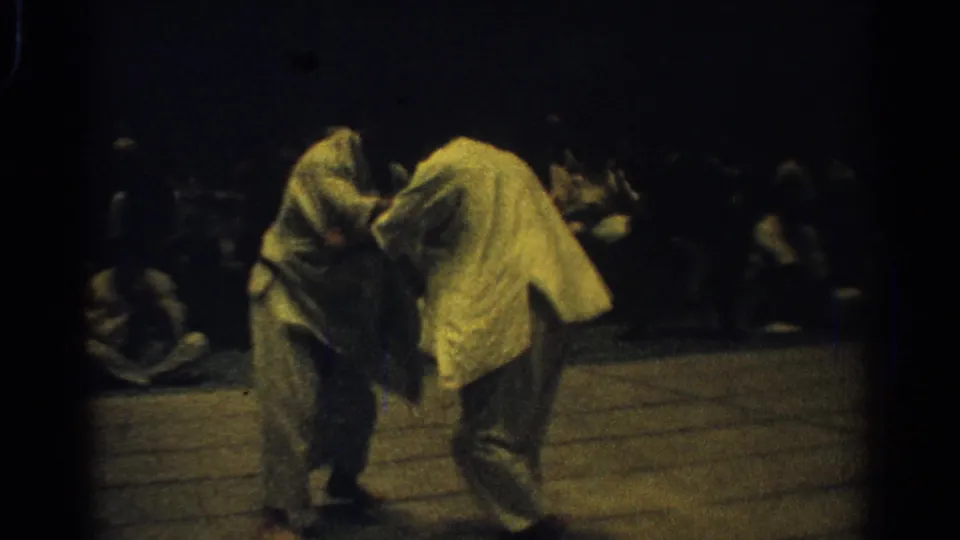 Two judo competitors in white gi lean into a standing grip during the West Covina championship footage.