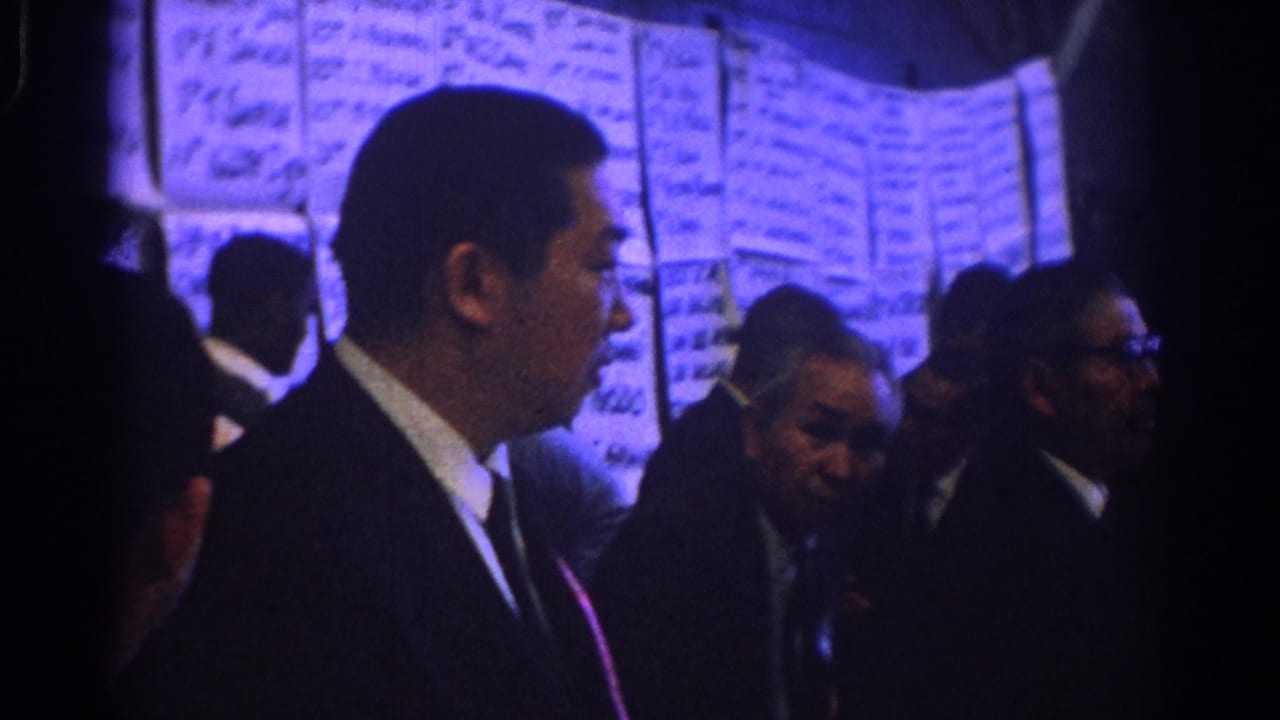 1966 West Covina conference footage shows suited men gathered near large handwritten wall charts under blue interior light.