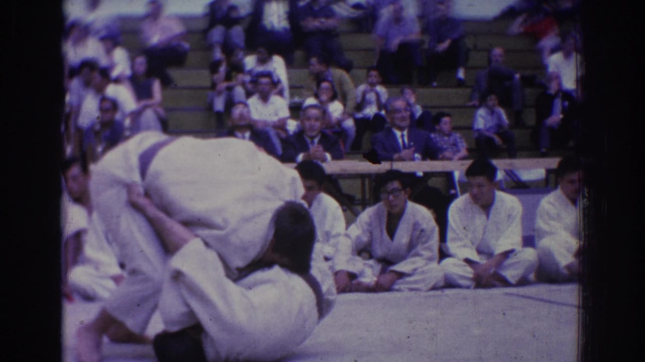 During the West Covina judo match, one athlete appears to lift or turn another while judges and spectators sit behind the mat.