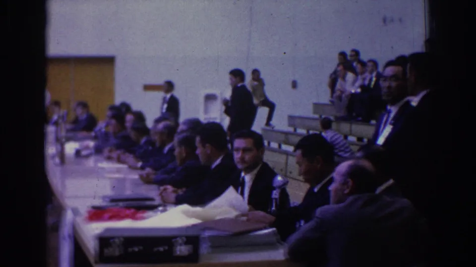 Officials in suits sit at a long table with papers and microphones as spectators watch from bleachers in West Covina, 1966.