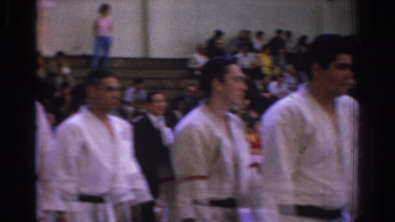 White-uniformed judo competitors move through the foreground while spectators sit on gym bleachers in the 1966 West Covina footage.
