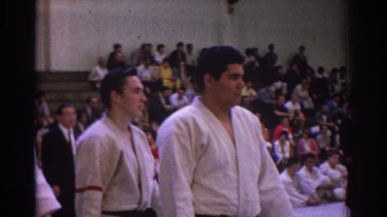Two karate competitors in white gi stand before bleachers in a crowded gymnasium.