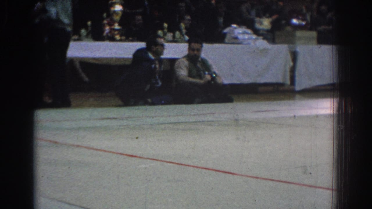 1966 West Covina judo venue view showing an empty section of mat, seated spectators, and officials near a long table.