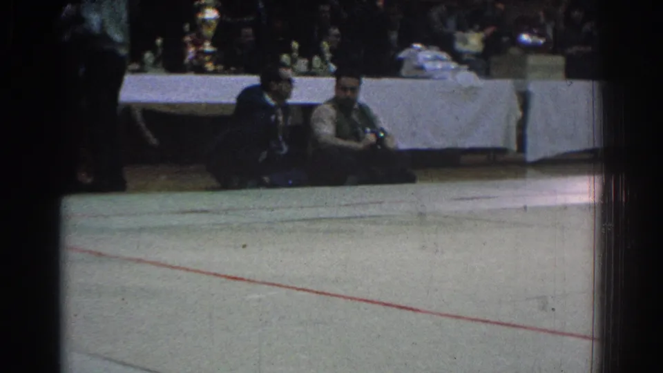 1966 West Covina judo venue view showing an empty section of mat, seated spectators, and officials near a long table.