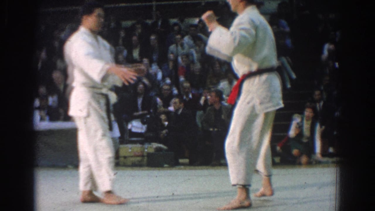 Two judo athletes in white gi face off on the West Covina mat, one wearing a dark belt and the other a red belt.
