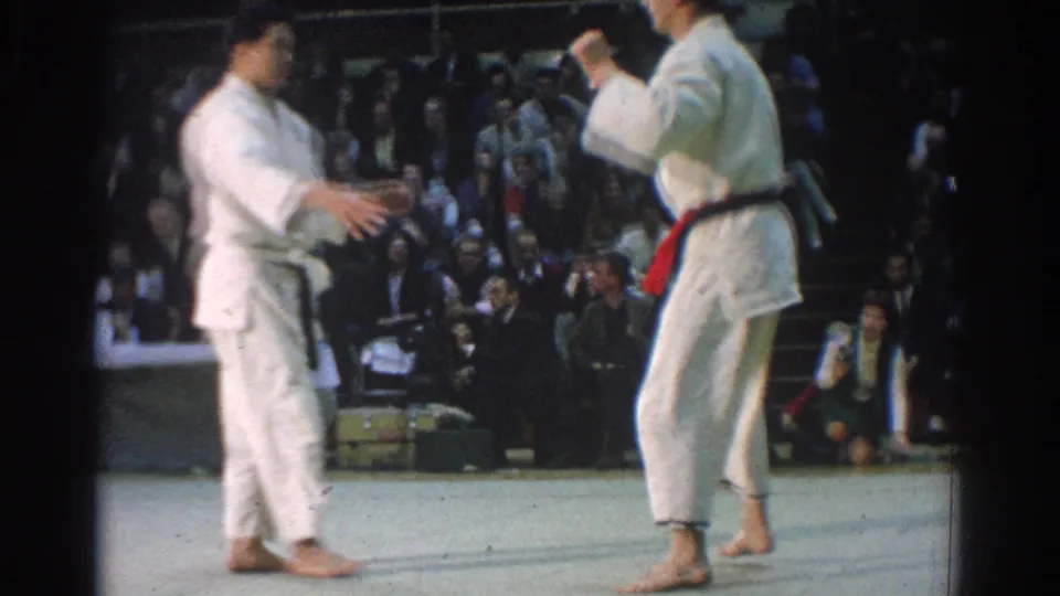 Two judo athletes in white gi face off on the West Covina mat, one wearing a dark belt and the other a red belt.