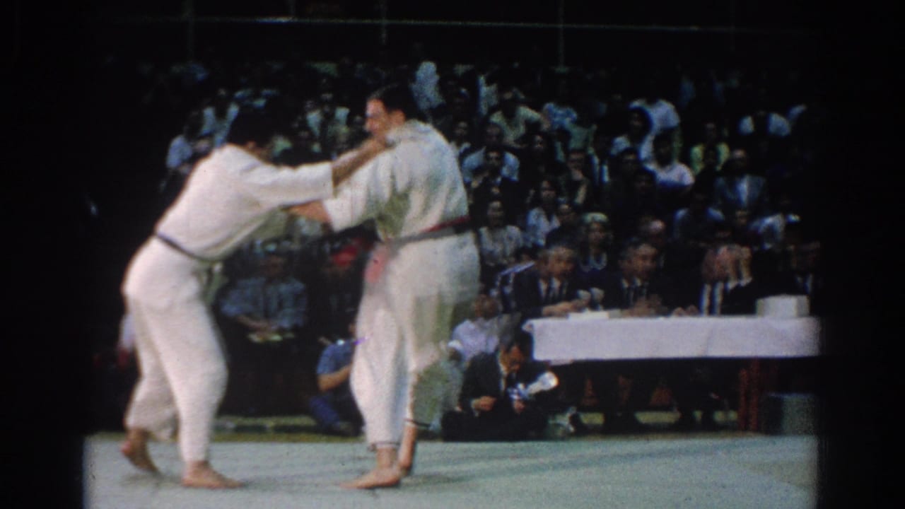 The judo athletes engage in a standing grip exchange during the 1966 West Covina match, with judges and spectators behind them.