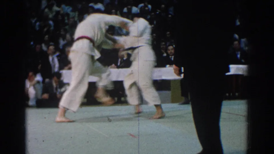 Two martial arts competitors clinch during a 1966 West Covina match, with an official partly blocking the spectator-shot view.