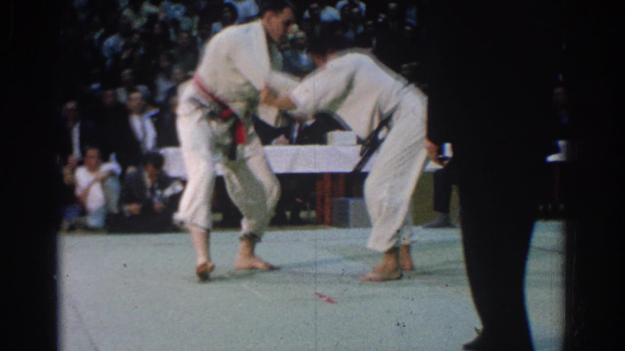 A red-belt competitor and a black-belt competitor grapple on the mat during the West Covina martial arts competition.