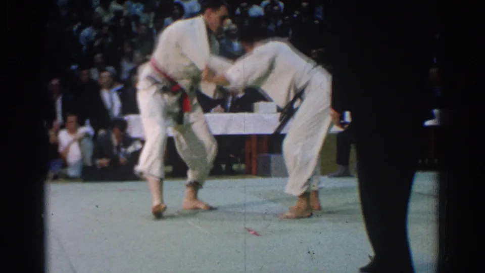 A red-belt competitor and a black-belt competitor grapple on the mat during the West Covina martial arts competition.