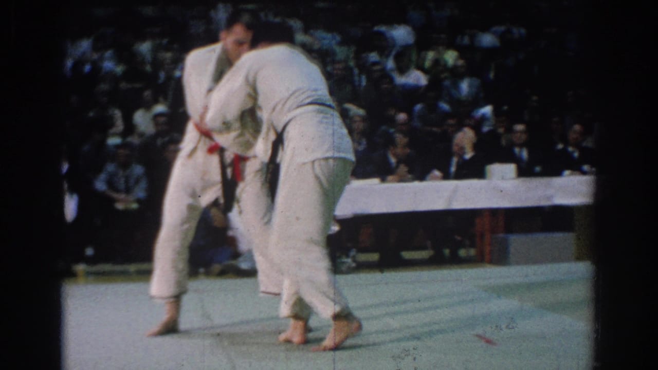 Close spectator view of two competitors grappling in white gis on a green mat at the 1966 West Covina event.
